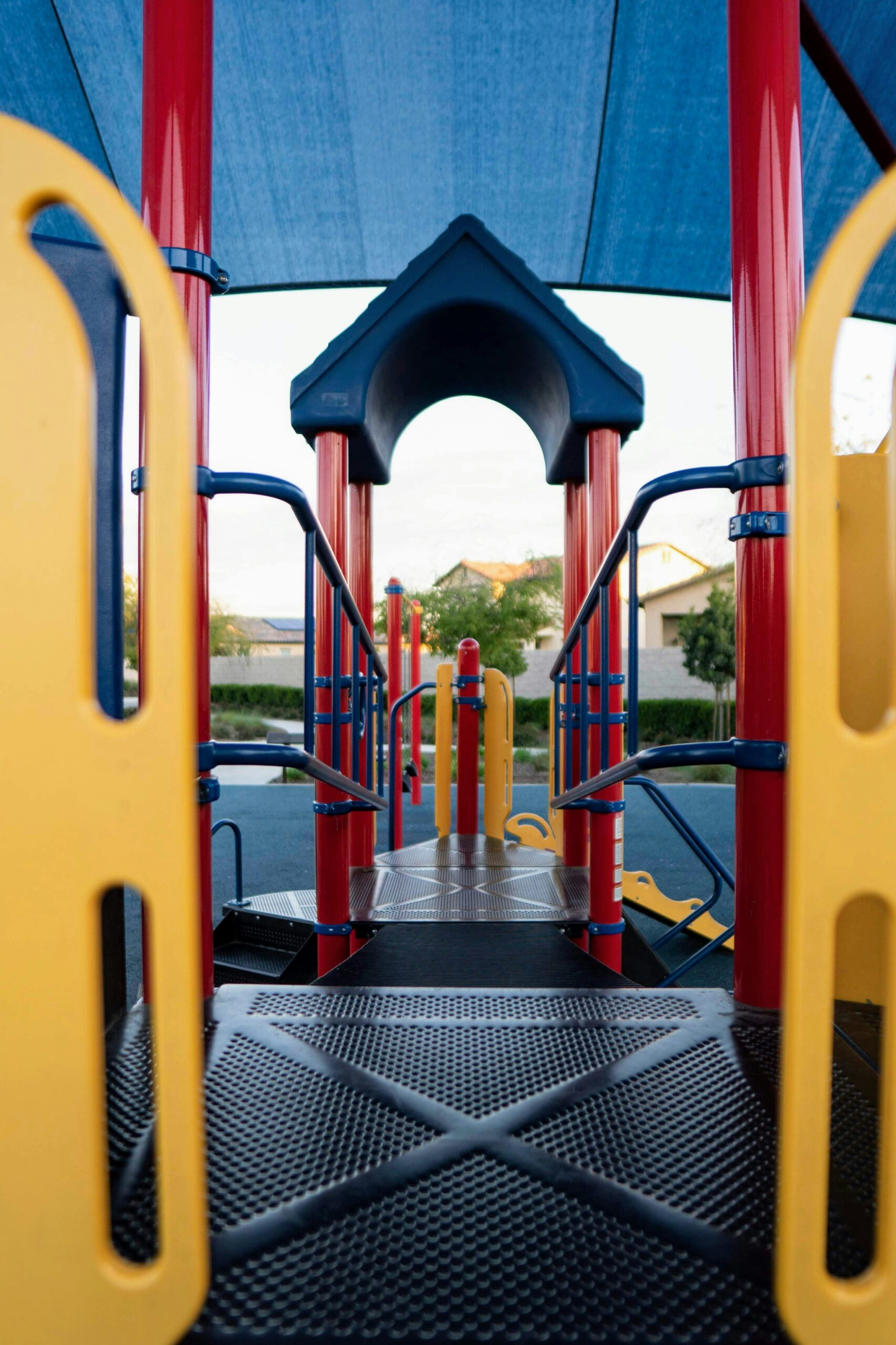 Blick auf eine farbenfrohe Spielplatzanlage mit roten, gelben und blauen Akzenten, bestehend aus einem Tunnel und einer Treppe, unter einem großen blauen Vordach.